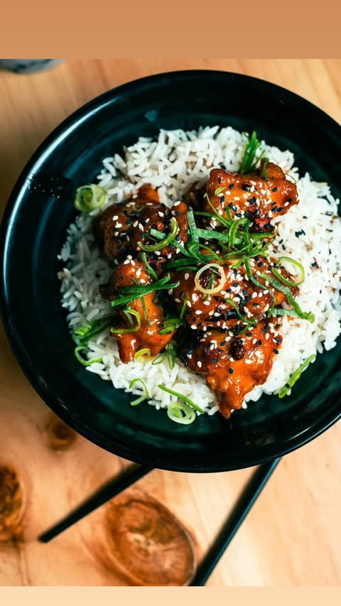Pollo en salsa picante sobre arroz con cebollín y ajonjolí